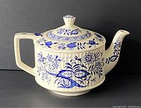 Full side view of the teapot showing handle, body, spout, and lid with blue onion floral pattern.