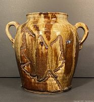 Front view of pottery vessel showing brown and tan glaze with leaf design and double handles.