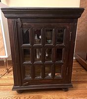 Front view of vintage wooden storage cabinet with glass paneled door showing grid design.