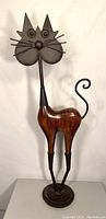 Full view of the cat sculpture showing wooden body and metal head, legs, tail, and base.