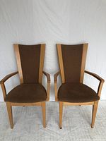 Front view of the pair of wooden dining armchairs with brown fabric upholstery, showing seat and backrest design.