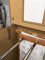 Open cabinet showing internal metal rods for hanging blueprints or large drawings, corkboard interior surfaces, partial lid opening mechanism.