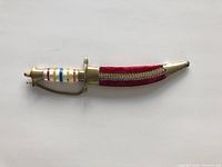 Top view of decorative dagger in red fabric sheath with brass fittings and multicolored striped handle