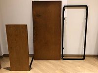 Desktop top, return, and frame standing upright against a wall on a wood floor.