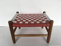 Front view of footstool showing woven red and white canvas top with solid wood frame and legs.