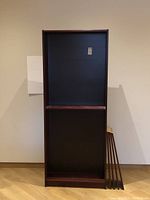 Front view of the maroon IKEA Billy bookcase with two shelves inserted and additional shelves leaning next to it.