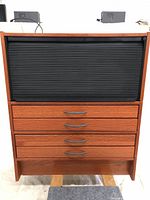 Front view of the IKEA EFFEKTIV office cabinet showing the top black roll-front door and four wooden drawers below with silver handles.