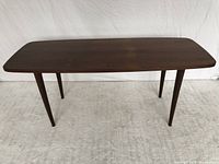 Front view showing the full table, four tapered legs and rectangular top with rounded edges in rosewood veneer.