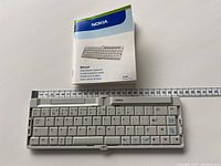 Folded Nokia Bluetooth folding keyboard next to measuring tape showing dimensions, original user manual visible in background