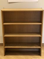 Front view of oak bookshelf cabinet showing three shelves and sliding panel tracks on the top two shelves.