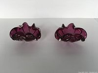 Side-by-side view of two magenta freeform Murano art glass bowls showing organic wave shapes.