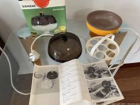 Complete Siemens TE07 egg boiler set displayed on glass table showing the unit, egg tray, power cord, instruction manual, and original box with product image.