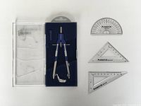 Overview of Staedtler geometry set including compass in case, two triangles, and protractor arranged on white background.