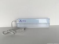 Front view of 14-inch fluorescent under cabinet light showing frosted acrylic lens, on/off switch, built-in mains outlet, and power cord with plug.