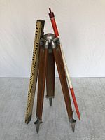 Full view of the Kern tripod with attached level rod and telescoping pole leaning against it on a carpeted surface