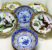 Full view of assorted plates showing hand painted dragons, floral motifs, and traditional figure designs with gold rims.