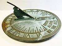 Close side view of sundial showing Roman numerals in relief and bird figure on gnomon.