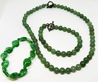 Three jade jewelry pieces including a bead choker, bead bracelet, and stretch heart bead bracelet laid out on white background.