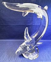 Clear crystal shark sculpture with a dynamic curled form on a rounded crystal base, displayed on a blue fabric background.