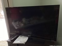 Samsung 40 inch TV on black stand with remote and manual lying on the stand.
