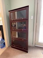 Front view of the barrister style bookcase showing four stacked shelves with glass panel doors and brass knobs.