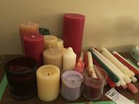 View of assorted pillar and taper candles in various colors and sizes, some in glass holders.