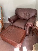 Brown leather overstuffed arm chair with matching ottoman positioned on carpeted floor.