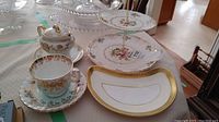 Overview of china serving items arranged on table, showing tiered plate, teacup and saucer, bone dish, and other pieces