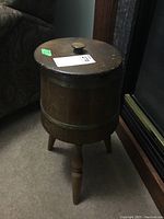 Full view of the wooden churn showing the three legs and round lid with knob, signs of surface wear visible.