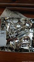 Top-down photo of assorted silver plate cutlery and serving utensils featuring floral April design on handles inside a tray.