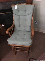 Front view of the wood frame rocker/glider chair with light blue-green fabric cushions showing button tufting and curved armrests.