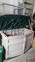 Weathered outdoor plastic storage chest with open green lid inside a garage or storage room.