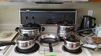 Full view of all cookware on stovetop including multiple covered pots, frying pan, kettle, and cups