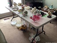 Top angle view of the Lifetime folding table showing white surface and various glass and ceramic items placed on it for storage only.