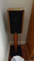 Front view of one speaker mounted on matching stand against wall