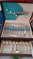 Original canteen case containing partial 1881 Rogers Lilac Time silverplate flatware set laid out with knives, forks, spoons, and serving utensils, showing floral pattern handles.