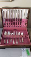Full view of Rogers silver plated cutlery in vintage wooden chest with pink velvet lining showing knives, forks, various spoons, ladle spoon and butter spreaders.