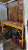 Front view of fully assembled scaffold showing steel frame, plywood deck, and caster wheels.