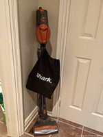 Full view of upright Shark Rocket vacuum cleaner standing in corner with attached accessory bag