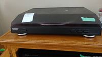 Front and side view of Sony turntable showing the lid, buttons, and feet.