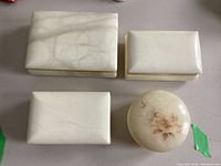 Top view of four lidded boxes: three rectangular, white with gold-tone frames and marble pattern, one round with floral design.