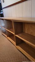 Photo of three connected wooden bookcases with two shelves each, showing natural wood grain and curved base, placed on carpet in front of wainscoted wall.