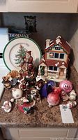 Wide view of entire lot showing ceramic house, Santa music box, assorted Christmas decorations and dog figurines on countertop.