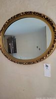 Full view of the oval mirror hanging on a wall showing the reflective surface and the gold-tone decorative frame.
