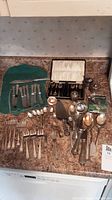 Overview of the assorted flatware laid out on a kitchen counter, showing knives, forks, spoons, and a box with small spoons inside.