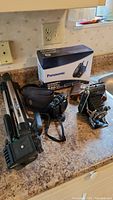 Full view of all items on countertop showing the Panasonic phone box, Thanges folding camera with case, Canon G10 camera, and tripod.