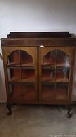 Front view of a wood display cabinet with two glass-paned doors and scalloped arch detailing