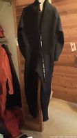 Photo of black full-length wetsuit hanging on a wooden door with tag visible, shows front side and zipper detail