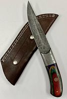 Hunting knife displaying Damascus steel blade and inlaid decorative wooden handle on leather sheath.