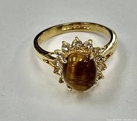 Front view of the ladies gold-plated ring showing brown cabochon stone center and halo of clear accent stones.